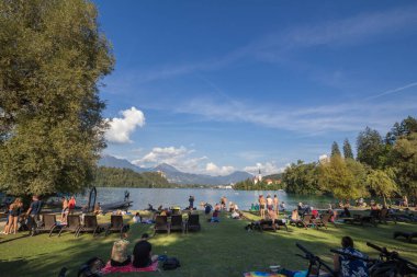 BLED, SLOVENIA - SEPTEMBER 11, 2021: İnsanlar Blejsko ostrvo kıyısında bir plajda yüzüyor, ya da Bled Gölü 'nde, Maria Kilisesi' nin varsayımıyla, ya da cerkev marijinega vnebovzetja ile kanlanmış bir adada yüzüyorlar. Katolik kilisesi.