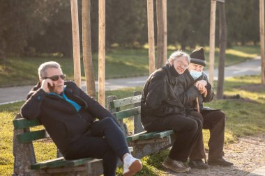 BELGRAD, SERBIA - 13 Mart 2021: Yaşlı arkadaşlar, oturmuş tartışıyorlar, gülümsüyorlar, mutlular, Coronavirus Covid 19 krizinde burun altına maske takıyorlar.