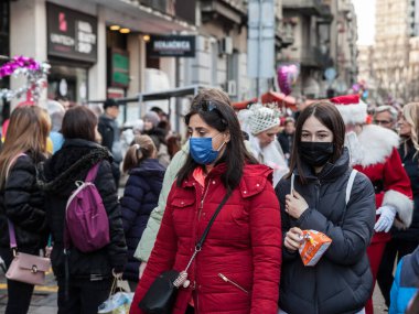 BELGRAD, SERBIA - 1 JANURY 2022: Kalabalığın ortasında yürüyen, Coronavirus Covid 19 krizinde yüz maskesi takan bir aile, bir anne ve kızı seçici bulanıklık