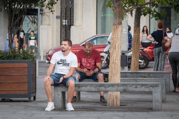 BELGRAD, SERBIA - 4 AĞUSTOS 2021: Akıllı telefonlarını izleyen ve başkent Sırbistan 'ın sokaklarındaki banklarda oturan iki genci seçici bulanıklık