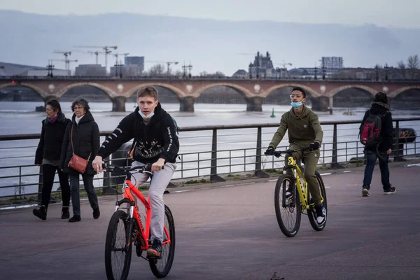 BORDEAUX, FRANCE - 20 Şubat 2022: Covid 19 Coronavirus sağlık krizi sırasında maskeler takarak Bordeaux, Fransa 'da bisikletle bisiklet süren iki genç erkek ve erkek çocuğu seçici bulanıklık