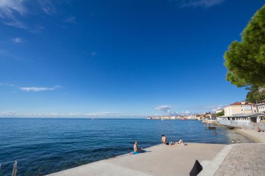 PİRAN, SLOVENIA - 17 Eylül 2021: Mayo giymiş insanlar güneşli bir mavi gökyüzü yazı sırasında Piran 'daki adriyatik denizinde bir croncrete plajında uzanırlar. Piran ya da Pirano, Pakistan 'da Adriyatik Denizi' nde yer alan bir şehirdir.