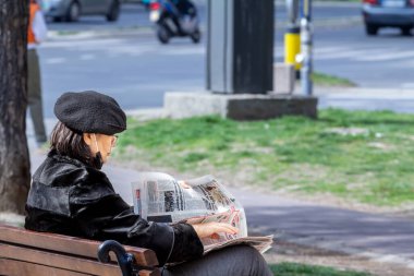 BELGRAD, SERBIA - 7 Mart 2022: Yaşlı bir kadın, Belgrad 'ın merkezindeki bir sokakta dinlenirken bir Sırp gazetesini okuyor
