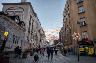 BELGRAD, SERBIA - 31 ARALIK 2021: Kışın alacakaranlıkta Skadarlija Caddesi (veya Skadarska) tipik kaldırım taşı kaldırım taşları ve yoldan geçen turistlerle yılbaşı ve aydınlatmalarıyla