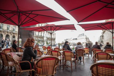 BORDEAUX, FRANCE - 24 FEBRUARY 2022: Bir müşteri, bir kadın, tek başına Fransız brasserisinin terasında oturan seçici bulanıklık, Bordeaux şehir merkezindeki De la bourse Meydanı 'nda