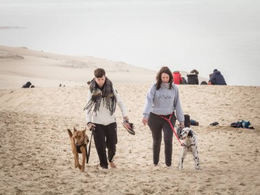 PILAT, FRANCE - 22 Şubat 2022: Pilat Dune 'da (Dune du Pyla) iki köpek gezdiren iki kadın ve kız üzerinde seçici bulanıklık. Pilat, ya da Pyla Dune Avrupa 'nın en büyük kum tepesidir, Arcachon Körfezi, Aquitaine