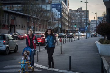 BELGRAD, SERBIA - 1 Nisan 2021: İki kadın, anne, bir çocuğu gezdiren, gülümseyen, kahve bardaklarını tutan, sıcak bir içecek içen seçici bulanıklık.
