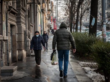 BELGRADE, SERBIA - JANUARY 15, 2022: Selective blur on Old woman walking in the streets of Belgrade wearing face mask protective equipement in winter during  Coronavirus Covid 19 crisis