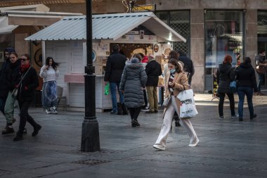 BELGRAD, SERBIA - 13 Şubat 2022: Coronavirus covid 19 krizi sırasında, solunum maskesi takmış, elinde alışveriş torbalarıyla koşuşturan seçici genç kadın