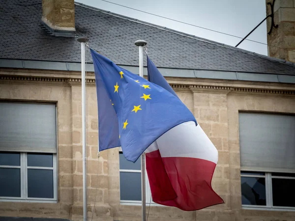 French flag and European Union flag standing in front of an old building, waiving. France is one of the main actors and members of the EU, and a founding member of European Union