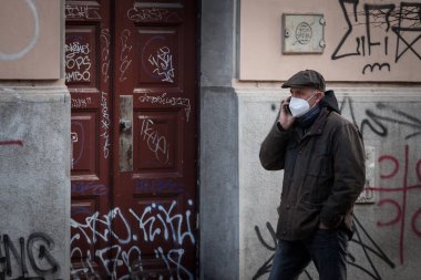 BELGRAD, SERBIA - 6 Mart 2021: Coronavirus covid 19 sağlık krizi sırasında Belgrad sokaklarında sartphone 'uyla telefon görüşmesi yapan yaşlı bir adamın solunum maskesi taktığı seçici bulanıklık