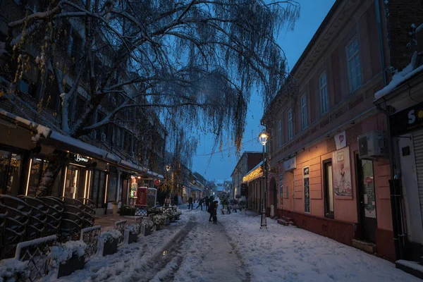 PANCEVO, SERBIA - 12 Aralık 2021: Banat bölgesinde kış karlı bir gecede, Pancevo 'nun ana caddesi ile ana caddesi arasında karda yürüyen insanlar üzerinde seçici bulanıklık