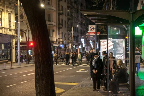 BELGRAD, SERBIA - 1 Ocak 2022: Coronavirus covid 19 krizi sırasında gece otobüs durağında toplu taşıma için solunum maskesi takan yaşlı bir kadının seçici bulanıklığı
