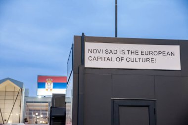 Novi Sad 'ın arkasında bir Sırp bayrağı bulunan 2022 yılı İngilizce kültürünün Avrupa başkenti olduğunu gösteren bir tabela üzerindeki seçici bulanıklık. Bu, Avrupa şehirlerinde kültürün yaygınlaştırılmasını amaçlayan bir etkinlik.