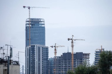 Bir emlak geliştirme alanında inşaat iskeleleri, beton ve beton cepheleri ve vinçleri olan gökdelen kulelerinden oluşan bir bina kompleksinin panoraması.