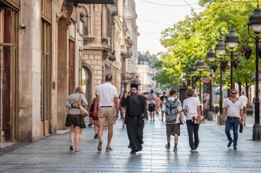 BELGRADE, SERBIA - JULY 23, 2022: Selective blur on a Serbian orthodox priest walking in the streets of Belgrade using his mobile phone, a smartphone, to go on the internet