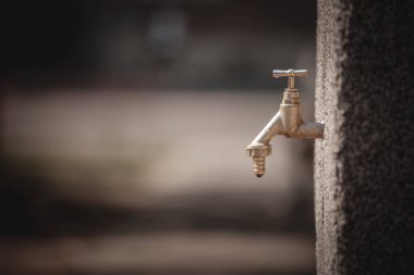 Selective blur on a dripping tap, a leaking faucet, old style, wasting water ressources in summer during a drought heatwave, aimed at distributing fresh drinking water, vertically standing on a public fountain
