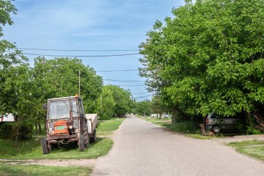 Typical countryside road in the village of Banatsko novo selo, a serbian village of the Banat region of Vojvodina, Serbia, with an old rusted tractor parked, waiting to plough fields
