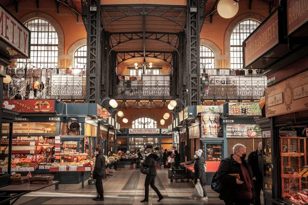 BUDAPEST, HUNGARY - FEBRUARY 26, 2022: Selective blur of people rushing with speed blur by stalls shop stand at the market of Nagyvasarcsarnok, the great Market hall of Budapest, symbol of Hungarian agriculture