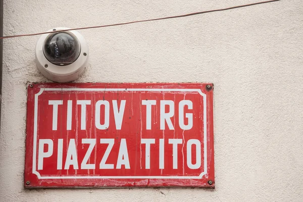 Bilingual street sign indicating Titov Trg in Slovenian and Piazza Tito in Italian, meaning Tito Street street, with a CCTV camera, obeying the slovenian biligualism minority laws in Koper. Tito is a communist yugoslav leader