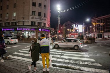 BELGRAD, SERBIA - 27 Kasım 2021: Seçici bulanıklık, bir çift, bir akşam boyunca Zebra geçidinde karşıdan karşıya geçmek için bekliyorlar ve sonbaharda Belgrad şehir merkezinde arabalarda hız bulanıklığı var..