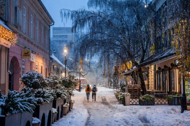 PANCEVO, SERBIA - 12 Aralık 2021: Banat bölgesinde kar yağışlı bir gecede, Pancevo 'nun ana caddesi ile ana caddesi arasındaki karda yürüyen çift, aşıklar için seçici bulanıklık