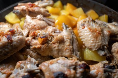 Kızarmış tavuk kanatları ve patatesler bir tavada pişirilir, yakın plan ve sığ alan derinliği vardır.