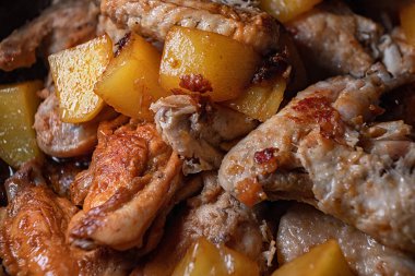 Kızarmış tavuk kanatları ve patatesler bir tavada pişirilir, yakın plan ve sığ alan derinliği vardır.