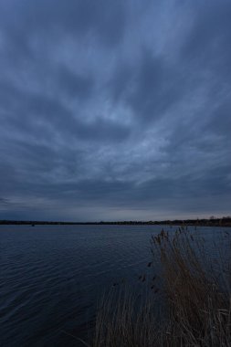 Gece geç saatlerde gölde. Ön planda ağaç dalları ile bulutlu ve bulutlu
