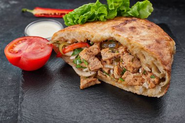 Giros, tavuk ve sebzeli pide, koyu bir arka planda.