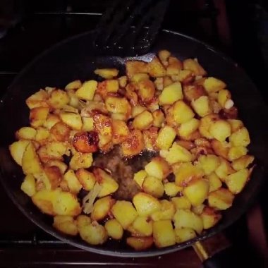Potatoes are fried in an old frying pan on a home stove. dark background