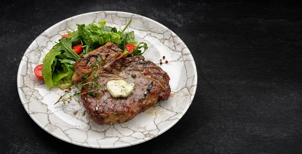 Filete a la parrilla con mantequilla, hierbas y tomates cherry en un plato blanco, sobre un fondo oscuro — Foto de Stock