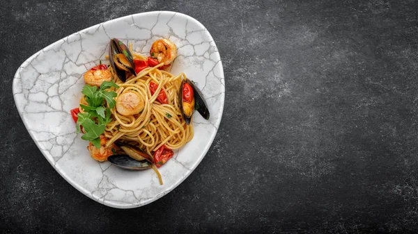 Espaguetis con mariscos, vieira, camarones, mejillones sobre un fondo oscuro con espacio para el texto Imagen de stock