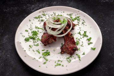 Izgara domuz pirzolası, soğan ve otlarla birlikte, koyu bir arka planda.