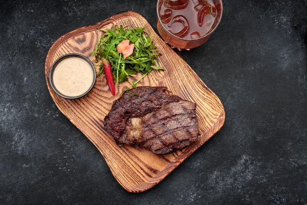 Gegrilltes Steak mit Sauce, Kräutern und einem Glas Whisky auf einem Holzbrett — Stockfoto