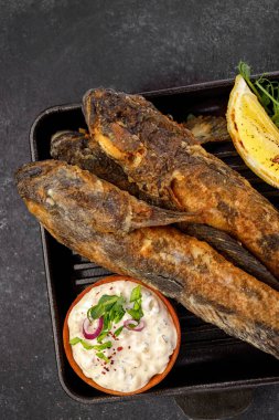 Koyu bir arka planda, limon ve otlarla kızartılmış balık Karadeniz kebabı.