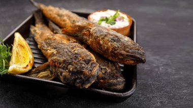 Koyu bir arka planda, limon ve otlarla kızartılmış balık Karadeniz kebabı.
