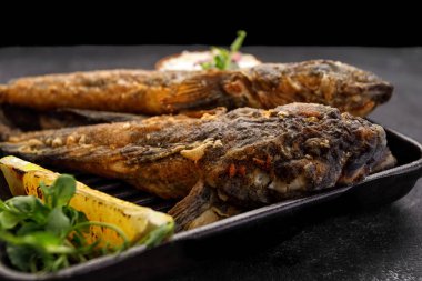 Koyu bir arka planda, limon ve otlarla kızartılmış balık Karadeniz kebabı.