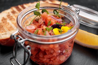 Somon tartartarlı tost, cam bir kavanozda, koyu bir arka planda.