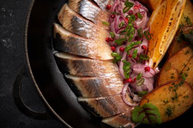 Kızartma tavasında fırında patates ve soğan ile turşulu ringa balığı.