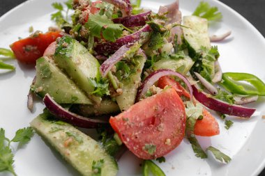 Salatalıklı, domatesli ve soğanlı yaz sebze salatası, beyaz tabakta, siyah arka planda.