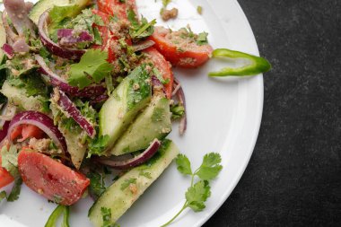 Salatalıklı, domatesli ve soğanlı yaz sebze salatası, beyaz tabakta, siyah arka planda.