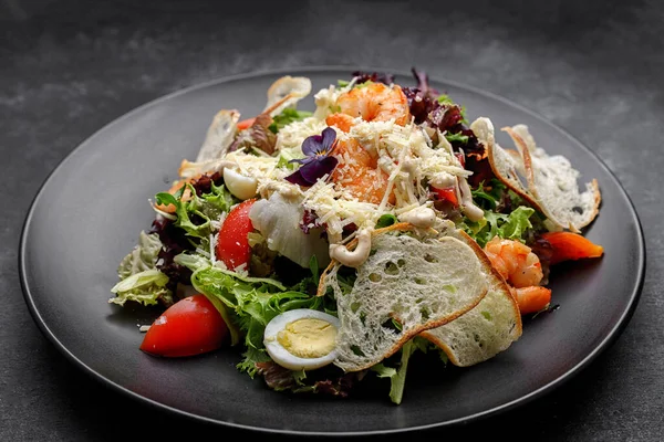 Caesar Salat Mit Garnelen Und Essbaren Blumen Auf Schwarzem Teller — Stockfoto