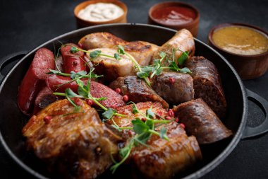 Tavada kızarmış et tabağı ve soslar, sosisler, kaburgalar, tavuk sosisi, domuz sosisi, siyah arka planda.