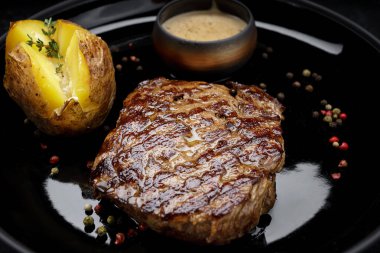 Fırında patates, hardal sosu ve biberli ızgara domuz eti. Bir tabakta, karanlık bir arka planda