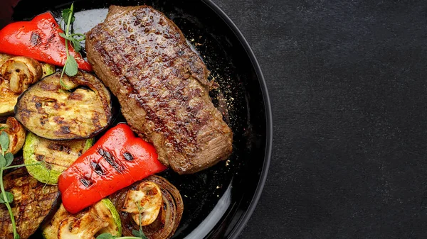 Sulu biftek ve ızgara sebze, tabakta baharatlar, koyu bir arka planda.