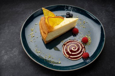 Portakallı ve ahududulu cheesecake, bir tabakta, koyu arkaplanda.