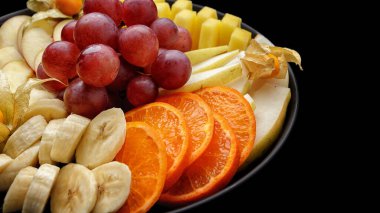 Tabakta dilimlenmiş meyve, tatlı. Karanlık bir arka planda. Mesajlaşmak için yer var. Üzüm, muz, portakal, armut, elma ananası