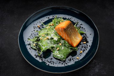 Izgara somon fileto, otlar ve fındıklı, bir tabakta, koyu bir arka planda. Metin için yer