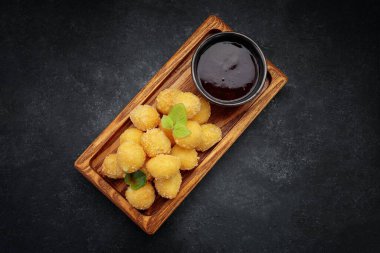 Tahta tahtada tatlı soslu peynirli nugget topları, koyu arkaplanda.